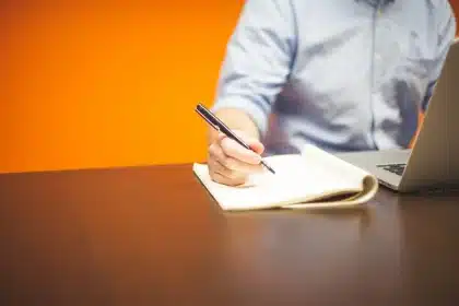 Hands holding a notepad and pen beside index cards on an office table