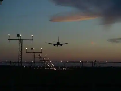 Silhouette of a large arch near a river with an airport runway in the distance
