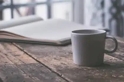 Hands filling a crossword grid with a pencil next to a mug and printed puzzles