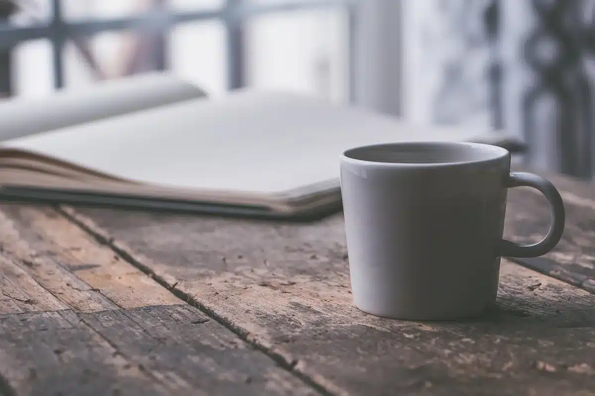 Hands filling a crossword grid with a pencil next to a mug and printed puzzles