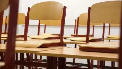 Outside a secondary school, backpacks and desks scattered, anonymous students in silhouette