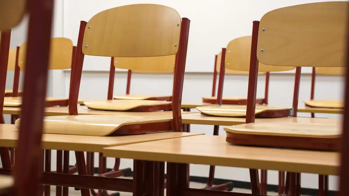 Outside a secondary school, backpacks and desks scattered, anonymous students in silhouette